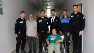 Görselde, bir koridorda poz veren bir grup insan görülüyor. Ortada tekerlekli sandalyede oturan genç bir kadın yer alıyor. Kadının etrafında beş polis memuru, bir takım elbiseli adam ve yaşlı bir adam bulunuyor. Herkes gülümseyerek kameraya bakıyor. Görsel, dayanışma ve toplumsal destek duygusunu yansıtıyor.