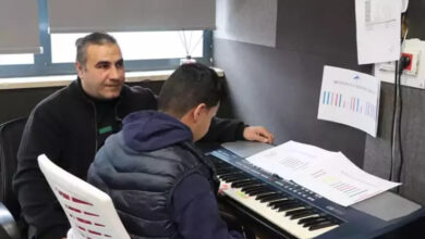 Öğretmen Süleyman Ekici piyano çalan erkek öğrencinin yanında bulunuyor.