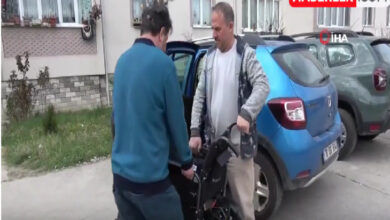 Görselde, bir apartmanın önünde park etmiş bir aracın yanında iki adam yer alıyor. Adamlar, aracın bagajından tekerlekli sandalye indiriyorlar. Arka planda birkaç araç daha park halinde ve apartman dairesi pencereleri görünüyor. Üst kısımda "Haberler.com" ve "İHA" logoları yer almakta. Görsel, engellilere yönelik yardım ve destek faaliyetlerini, özellikle bireysel girişimlerle gerçekleştirilen sosyal sorumluluk projelerini yansıtıyor.