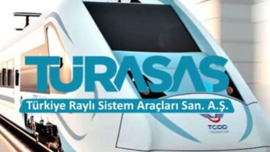 Görselde modern ve aerodinamik tasarıma sahip beyaz bir yüksek hızlı tren bulunuyor. Üzerinde büyük harflerle "TÜRASAŞ" yazısı yer almakta. Altında ise "Türkiye Raylı Sistem Araçları San. A.Ş." ifadesi görülüyor. Trenin ön kısmında TCDD (Türkiye Cumhuriyeti Devlet Demiryolları) logosu mevcut. Arka planda ise hafif bulanık bir tren istasyonu veya tünel çıkışı hissi veren bir görüntü bulunuyor.
