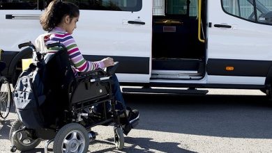 Görselde, tekerlekli sandalyede oturan genç bir kız, kapısı açık olan engelli erişimine uygun bir okul servisine binmek üzere. Servis aracı beyaz renkte ve yerde bir rampa sistemi görünmüyor ancak erişim sağlanacağı izlenimi veriliyor. Görsel, engelli bireylerin eğitime erişimini kolaylaştıran taşımalı eğitim uygulamasını yansıtıyor.