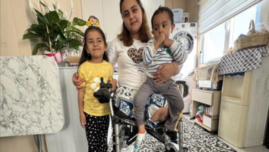 Ebru Çelikkol tekerlekli sandalyede oturuyor, oğlunu kucağında tutuyor ve kız çocuğu yanında ayakta bulunuyor.