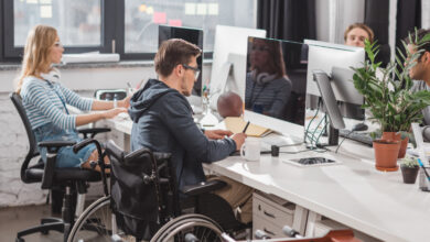 Fotoğrafta bir ofis ortamında çalışan insanlar yer alıyor. Çalışan işçilerden bir tanesi tekerlekli sandalye kullanan engelli birey olması dikkat çekiyor.