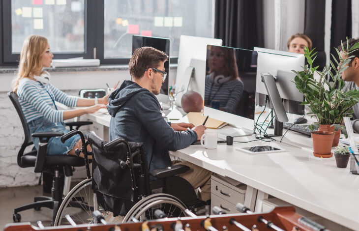 Fotoğrafta bir ofis ortamında çalışan insanlar yer alıyor. Çalışan işçilerden bir tanesi tekerlekli sandalye kullanan engelli birey olması dikkat çekiyor.