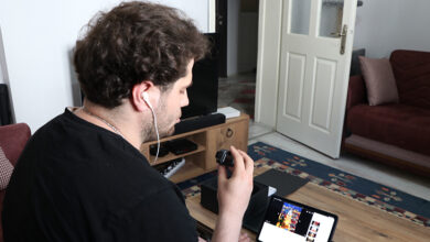 Fotoğrafta, Ömer Faruk Bektaş bir bilgisayarın başında oturmuş elinde tuttuğu mikrofona doğru konuştuğu görülmektedir.