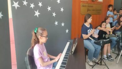 Görselde, genç bir kız dijital piyano çalarken görülüyor. Üzerinde mor bir tişört ve saçlarında yeşil toka olan bu kız, dikkatle tuşlara odaklanmış. Arka planda gitar çalan ve ritim tutan diğer öğrenciler yer alıyor. Duvarda beyaz yıldız figürleri ve Atatürk’ün bir sözüyle birlikte büstü dikkat çekiyor.