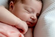 Fotoğrafta bir bebek var. Bebeğin üzerinde ince bir örtü olduğu görülmektedir. Bebek hafif yana dönük şekilde uyuyor olduğu düşünülmektedir.