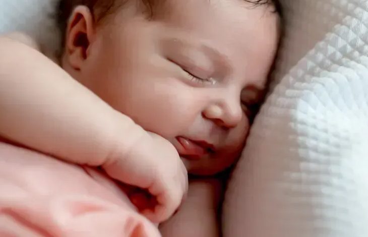 Fotoğrafta bir bebek var. Bebeğin üzerinde ince bir örtü olduğu görülmektedir. Bebek hafif yana dönük şekilde uyuyor olduğu düşünülmektedir.