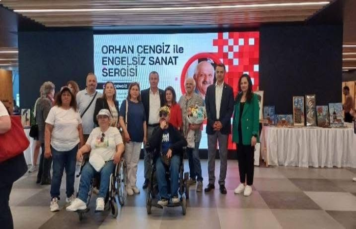 Önde tekerlekli sandalye kullanan iki erkek katılımcı ile arkada bulunan Ressam Orhan Cengiz ve katılımcılar ayakta poz veriyor.