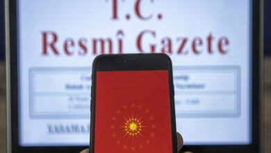 Görselde, ön planda bir cep telefonu ekranı yer almakta. Ekranda kırmızı zemin üzerinde Türkiye Cumhurbaşkanlığı forsunun simgesi görülüyor. Arka planda ise bir dizüstü bilgisayar ekranında “T.C. Resmî Gazete” başlığı dikkat çekiyor. Görsel, Türkiye’de alınan resmî kararların ve duyuruların yayımlandığı Resmî Gazete’ye dijital erişimi temsil ediyor.