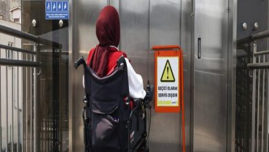 Görselde bir asansörün önünde duran akülü tekerlekli sandalye kullanan engelli birey yer alıyor. Asansörün önüne katılan tabelada geçici olarak hizmet dışı olduğu ifadesi belirtilmektedir.