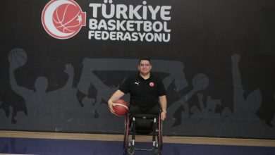 Görselde, Türkiye Basketbol Federasyonu logosunun önünde bir basketbol sahasında poz veren bir erkek yer alıyor. Tekerlekli sandalyede oturan bu kişi, elinde bir basketbol topu tutmakta ve milli takım formasını giymiş durumda. Arka planda spor temalı bir siluet duvar resmi bulunuyor.