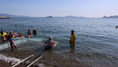 Raylı sistem sezlonguna oturan bedensel engelli kadın denize girerken etrafında vatandaşlar bulunuyor.