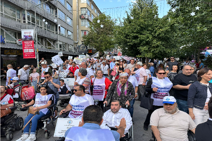 Görselde, Türkiye’nin dört bir yanından gelen engelli bireyler, yakınları ve aktivistler büyük bir yürüyüş gerçekleştiriyor. Kalabalık, “Engelliler sesleniyor: Haklarımızı istiyoruz” yazılı tişörtler ve dövizler taşıyor. Tekerlekli sandalyeli yurttaşlar ön safta yer alırken, kalabalık bir destekçi grubu arkalarında yürüyor.