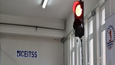 Kapalı bir mekanda trafik lambası yer alıyor. Trafik lambasında kırmızı ışık yanıyor. Lambanın arka planında ise duvarlara asılı bir bayrak ile lambanın tam arkasında bir yazı yer alıyor.