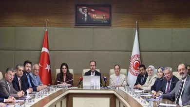 Bu fotoğraf, Türkiye Büyük Millet Meclisi'nde (TBMM) gerçekleşen resmi bir komisyon toplantısını gösteriyor. Masanın başında yer alan kişi, AK Parti İzmir Milletvekili Mehmet Muharrem Kasapoğlu. Arka planda Türk bayrağı, TBMM bayrağı ve Atatürk portresi yer alıyor. Katılımcılar resmi giyimli, çoğunluğu milletvekili ya da bürokratlardan oluşuyor. Masada belgeler, mikrofonlar, isimlikler ve su bardakları bulunuyor. Genel atmosfer ciddi, resmi ve kurumsal.