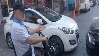 Beyaz ve siyah otomobillerin kaldırım geçitinin önünde yakın park edilmesi sebebiyle motosikletli erkek sürücü kaldırımda bekliyor.