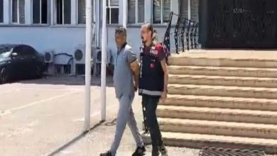 Görselde, elleri arkadan kelepçelenmiş bir suçlu ile bir polis memuru yan yana yürüyor. Polis memuru, suçlunun kaçmaması için onun kolunu tutuyor.