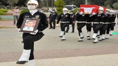 Görselde, cenaze töreni sırasında görev şehidi bir polis memuru için resmi tören düzenleniyor. Önde yürüyen bir polis memuru, hayatını kaybeden meslektaşının fotoğrafını taşıyor. Arkasında ise altı polis memuru, Türk bayrağına sarılı tabutu omuzlarında taşıyor. Hepsi resmi kıyafetli, beyaz kask ve eldiven takmış durumda. Tören ciddiyet ve saygı içinde ilerliyor; çevrede bazı insanlar töreni izliyor. Bu kare, hem hüzün hem de onur dolu bir vedayı yansıtıyor.