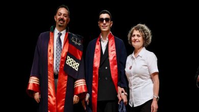 Görselde bir mezuniyet töreni sahnesi yer almakta. Ortada siyah gözlük takan ve cübbe giymiş bir genç yer alıyor; elinde beyaz bastonu var, bu da onun görme engelli olduğunu gösteriyor. Solunda yine cübbe giymiş bir akademisyen, sağında ise beyaz gömlekli bir kadın bulunuyor. Üçü de gülümsüyor ve mutlulukları yüzlerinden okunuyor.