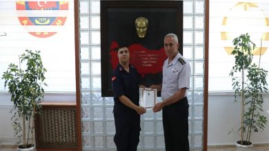 Görselde, engelli bir birey ile askeri üniforma giymiş bir komutan yan yana duruyor. Komutan, engelli bireye plaket verirken görüntülenmiş. Fotoğrafın, resmi bir törende çekildiği anlaşılmaktadır.