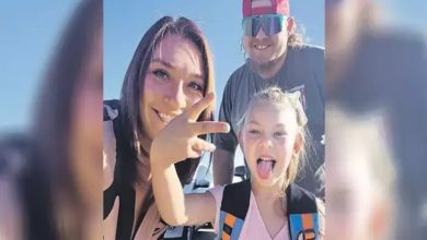 Görselde açık havada, güneşli bir günde çekilmiş mutlu bir aile fotoğrafı yer alıyor. Ön planda küçük bir kız çocuğu dili dışarıda, neşeli bir ifadeyle kameraya bakıyor ve el hareketi yapıyor. Arkasında bir kadın ve bir erkek yer alıyor; kadın gülümsüyor, erkek ise güneş gözlüğü ve kırmızı şapkasıyla poz veriyor. Her üçü de samimi ve enerjik bir anı paylaşıyor. Arka planda arabalar ve açık mavi gökyüzü dikkat çekiyor.