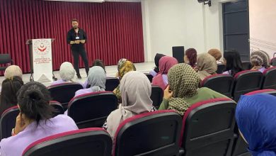 Sahnede bulunan eğitmen erkek, izleyici koltuklarında bulunan personellere hitap ediyor.