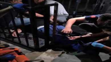 Görselde birkaç görevli, yerde hareketsiz yatan bir kişiye müdahale ediyor. Çevrede metal engelli asansörüne ait korkuluklar ve karanlık bir ortam dikkat çekiyor. Olayın acil müdahale gerektiren bir kaza sonrası gerçekleştiği izlenimi var.