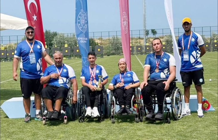 Görselde, Beykoz Belediyesi Spor Kulübü’nün tek bedensel engelli takımı olan Para Okçuluk ekibi tekerlekli sandalyeleri üzerinde oturarak yan yana almış oldukları madalyaları boyunlarına asılı bir şekilde fotoğraf için poz veriyorlar.
