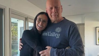 Görselde bir kadın ve bir erkek, ev ortamında birbirlerine sarılarak poz veriyor. Kadın gülümserken erkek Bruce Willis, gözlerini kapatmış. Arkada geniş cam kapılar ve iç mekân dekorasyonu görülüyor.