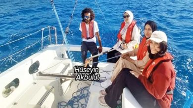 Görselde, deniz üzerinde seyreden bir yelkenlide dört kişi yer alıyor. Hepsi can yeleği giymiş ve teknenin içinde oturuyor. Ön planda üç kadın, arka tarafta ise dümeni tutan ve adı görselde “Hüseyin Akbulut” olarak belirtilen bir erkek bulunuyor. Masmavi deniz ve açık hava, keyifli bir yelken yolculuğu atmosferi oluşturuyor.