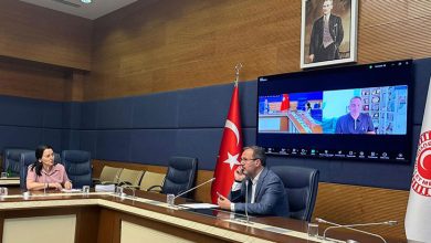 TBMM Engelli bireylerin Sorunlarının Araştırılması Komisyonu'nda salonunda, masada sağda Dr. Mehmet Muharrem Kasapoğlu solda ise Ayşe Sarı oturuyor. Masada mikrofon, su bardağı ve çeşitli belgeler yer almakta. Masanın arkasında, büyük bir ekran üzerinde bir Zoom toplantısı açık. Ekranda Mehmet Kızıltaş toplantıya dahil olmuş. Masanın sağ tarafında, Türkiye Büyük Millet Meclisi (TBMM) amblemini taşıyan bir bayrak bulunuyor.