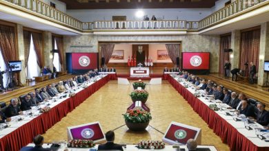 Türkiye Büyük Millet Meclisi büyük toplantı salonunda, TBMM Başkanı Numan Kurtuluş'un yönettiği toplantıda farklı siyasi partilerden gelen çok sayıda milletvekili ve bürokrat U şeklinde dizilmiş uzun masalarda katılımcı olarak bulunuyor.