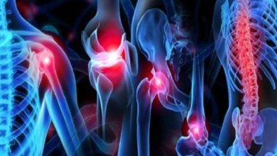 Görselde, insan iskelet sisteminin bilgisayar ortamında hazırlanmış renkli bir temsili görülüyor. Omuz, diz, kalça ve omurga gibi eklem bölgeleri kırmızıyla vurgulanmış, bu da ağrı veya sorunlu bölgeleri işaret ediyor. Arka plan koyu, kemikler mavi tonlarda gösterilmiş.