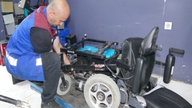 Erkek personel akülü tekerlekli sandalyenin ön kısmını tamir ediyor.