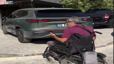 Görselde, elektrikli tekerlekli sandalye kullanan bir birey kaldırıma çıkmak isterken, kaldırımın girişini kapatan bir aracın (TOGG) yüzünden ilerleyemiyor. Kişi, elinde telefonuyla bu duruma tepkisini gösteriyor gibi görünüyor. Araç, engelli bireyin geçiş hakkını engelleyerek ciddi bir erişilebilirlik sorununa yol açıyor.