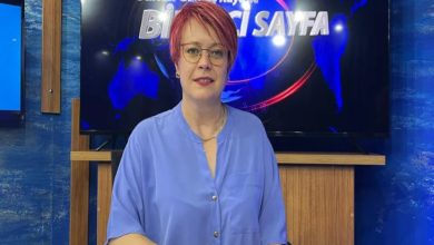 Görselde kısa saçlı, gözlüklü ve açık mavi gömlek giymiş bir kadın stüdyo ortamında oturuyor. Arkasında “Sultan Gümüş Kayalı ile Birinci Sayfa” yazısının yer aldığı bir ekran var. Masada beyaz bir fincan bulunuyor.