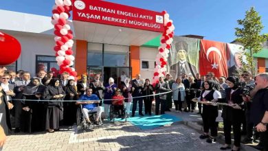 Görselde, **Batman Engelli Aktif Yaşam Merkezi Müdürlüğü**’nün açılış töreni görülüyor. Kırmızı-beyaz balonlarla süslenmiş giriş kapısının önünde kalabalık bir grup toplanmış. Kurdele kesimi için hazırlık yapılmış; ön sırada tekerlekli sandalyede iki engelli birey yer alıyor. Arkada büyük Atatürk ve Türk bayrağı afişleri dikkat çekiyor. Sağda ise kadın görevliler ikramlık tepsiler taşıyor.