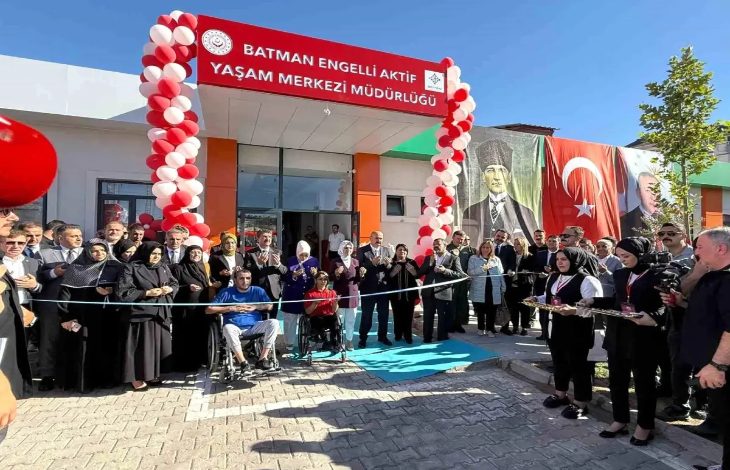 Görselde, **Batman Engelli Aktif Yaşam Merkezi Müdürlüğü**’nün açılış töreni görülüyor. Kırmızı-beyaz balonlarla süslenmiş giriş kapısının önünde kalabalık bir grup toplanmış. Kurdele kesimi için hazırlık yapılmış; ön sırada tekerlekli sandalyede iki engelli birey yer alıyor. Arkada büyük Atatürk ve Türk bayrağı afişleri dikkat çekiyor. Sağda ise kadın görevliler ikramlık tepsiler taşıyor.