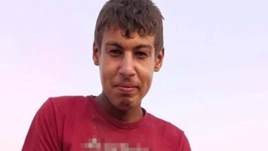 Görselde, açık havada çekilmiş bir fotoğraf yer alıyor. Kısa saçlı, genç bir erkek çocuğu Halil Abay kırmızı tişört giymiş şekilde kameraya doğru hafif bir gülümsemeyle bakıyor. Arka plan sade, açık gökyüzü görünüyor. Tişörtteki yazı bulanıklaştırılmış.