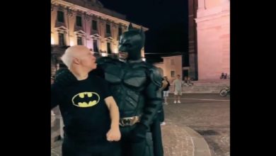 Görselde gece saatlerinde, tarihi bir şehir meydanında çekilmiş duygusal bir an yer alıyor. Siyah Batman tişörtü giymiş, beyaz saçlı Down sendromlu bir birey, tam teçhizatlı Batman kostümü giymiş bir kişiyle yan yana duruyor. Batman, kolunu sevgiyle bireyin omzuna dolamış; ikisi de birbirine sıcak ve samimi bir şekilde bakıyor. Arka planda tarihi yapılar ve birkaç kişi görülüyor. Bu kare, özel bir sürprizin ve dokunaklı bir karşılaşmanın etkileyici anını yansıtıyor.