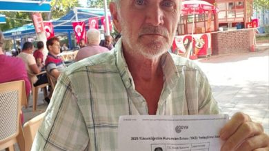 Görselde yaşlı bir adam açık havada, masa başında oturmuş elinde bir belge tutuyor. Belgede ÖSYM logosu ve sınav yerleştirme sonuç bilgileri görülüyor. Arka planda dış mekânda oturan başka insanlar ve kafeterya ortamı yer alıyor. Adamın yüz ifadesi ciddi.