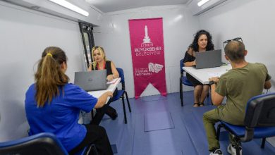 Görselde, İzmir Büyükşehir Belediyesi’ne ait **Meslek Fabrikası Mobil İstihdam Aracı** içinde dört kişi karşılıklı masalarda oturmuş şekilde görülüyor. İki belediye personeli, karşılarındaki bireylerle laptoplar üzerinden görüşme yapıyor. Aracın arka kısmında **İzmir Büyükşehir Belediyesi** ve **Meslek Fabrikası** logolarının yer aldığı pembe bir afiş bulunuyor.