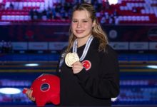 Milli para yüzücü Defne Kurt, şampiyona maskotunu sağ elinde tutarken boynunda duran altın madalyayı sol eliyle tutup gülerek poz veriyor.