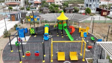 Görselde rengarenk oyun gruplarının yer aldığı modern bir çocuk parkı görülüyor. Parkta kaydıraklar, salıncaklar ve tırmanma alanları bulunuyor. Salıncaklar ve ekipmanlar engelli çocuklar için de uygun şekilde tasarlanmış. Parkın çevresinde binalar ve yeşil alanlar dikkat çekiyor.