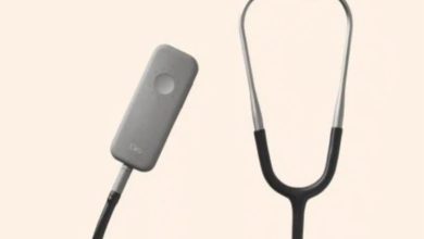 Görselde modern tasarımlı, teknolojik özellikli bir stetoskop bulunuyor. Sol tarafta dikdörtgen şeklinde bir sensör cihazı, sağda klasik stetoskop kulaklık kısmı görülüyor. Arka plan sade ve açık renkli.