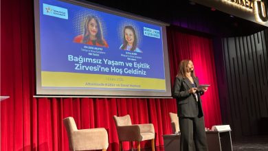 Görselde bir sahne ortamı görülüyor. Arkada kırmızı perde önünde büyük bir ekran bulunuyor. Ekranda “Bağımsız Yaşam ve Eşitlik Zirvesi’ne Hoş Geldiniz” yazısı yer alıyor ve konuşmacıların fotoğrafları ile isimleri gösterilmiş. Sahnenin önünde iki koltuk ve bir sehpa var. Önde ise bir kadın sunucu mikrofon ve tabletle konuşma yapıyor. Mekân Altunizade Kültür ve Sanat Merkezi olarak belirtilmiş.