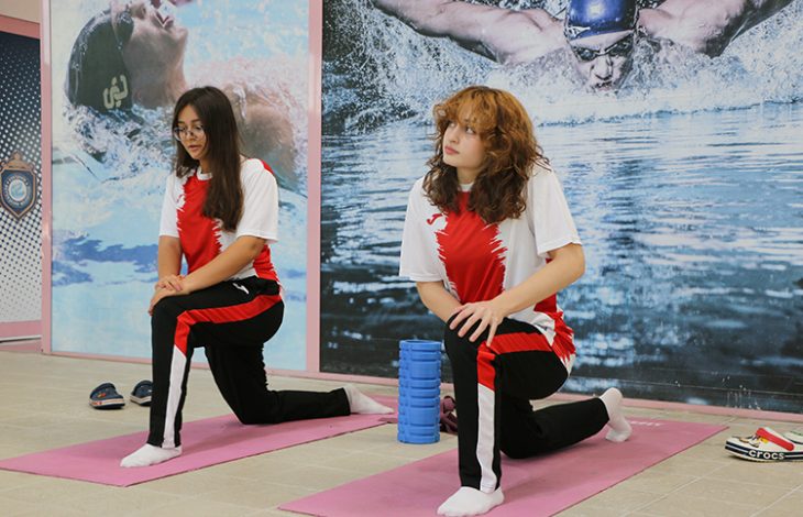 İdil Bengisu Tunçbilek ve Irmak Çetinkaya, spor salonunda dizlerinin üstünde durarak idman yapıyor.