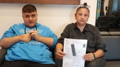 Görselde iki kişi bir koltukta yan yana oturuyor. Soldaki genç mavi bir sweatshirt giymiş, sağdaki kadın ise elinde engelli raporu belgesi tutuyor. Belgenin bazı bölümleri gizlenmiş. Arka planda iç mekân detayları görülüyor.