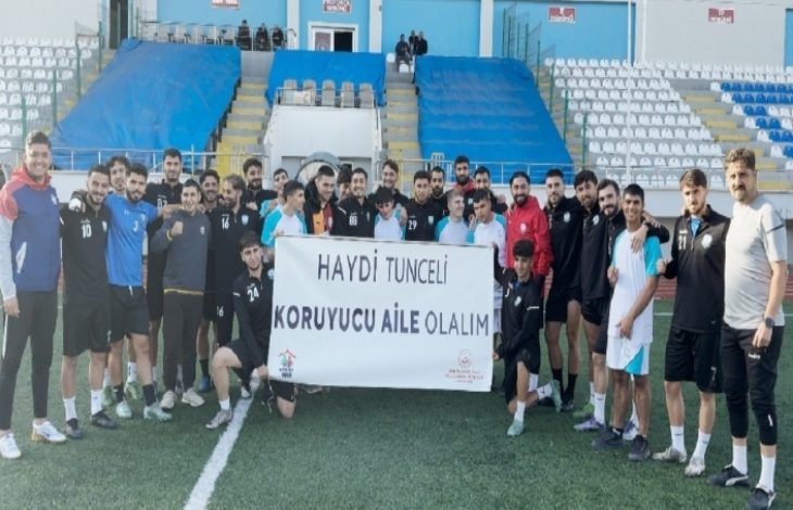 Görselde futbol sahasında bir grup sporcu ve genç birlikte poz veriyor. Ellerinde “Haydi Tunceli Koruyucu Aile Olalım” yazılı bir pankart tutuyorlar. Arka planda tribünler ve saha düzeni görülüyor. Katılımcılar gülümseyerek kameraya bakıyor.